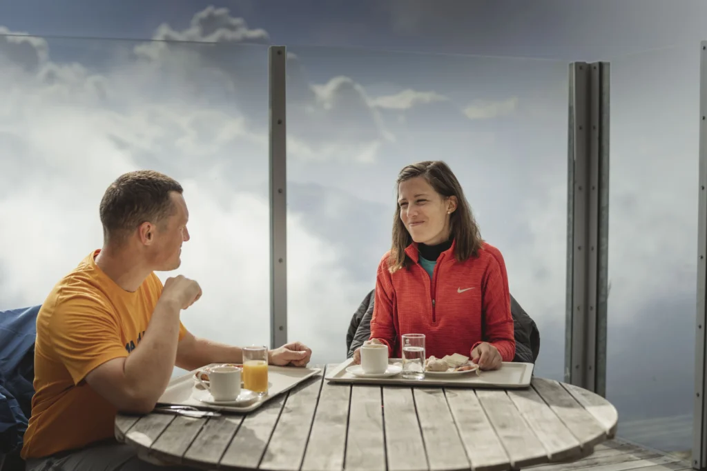 Sonnenaufgangsfahrt Eggishorn mit Paar beim Frühstück auf der Terrasse über dem Wolkenmeer in der Aletsch Arena